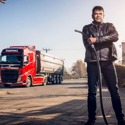 Petr Šišlák stands in the foreground holding a petrol pump with a Volvo truck behind him