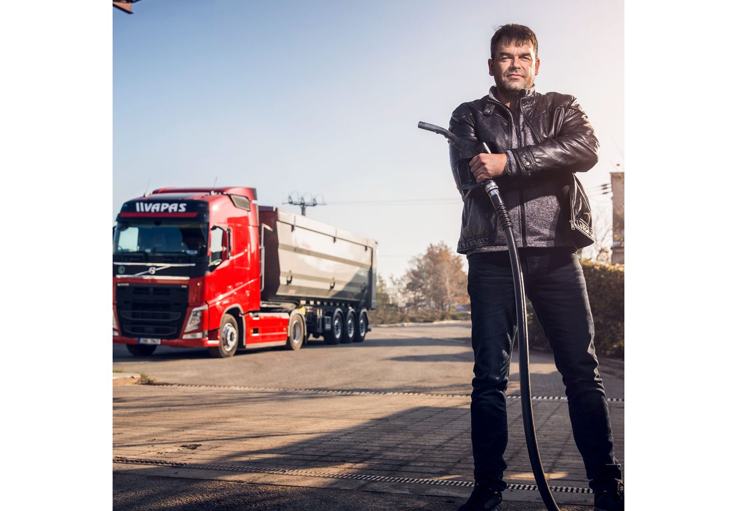 Petr Šišlák se encuentra en primer plano, sosteniendo un surtidor de gasolina con un camión Volvo detrás de él.