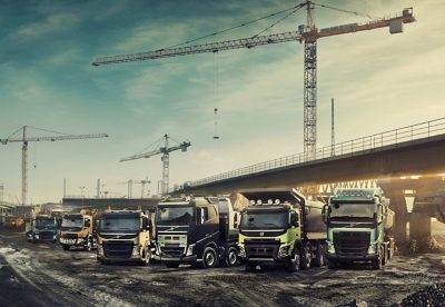 Six Volvo Group trucks lined up at a construction site underneath a bridge