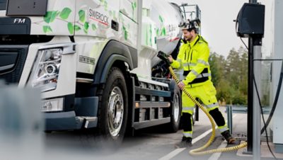 A man in high visibility clothing carries a charging cable to the Volvo FM electric truck 
