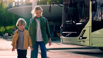 Two children crossing a street with a bus in the background.