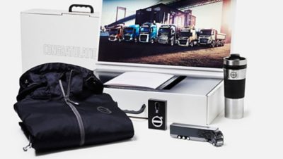 Volvo Group merchandise: jacket, coffee mug, Volvo truck toy, lighter, picture of Volvo trucks