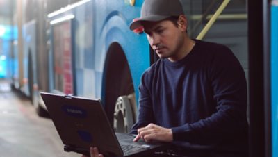 En værkstedstekniker sidder med en bærbar computer foran en bus.