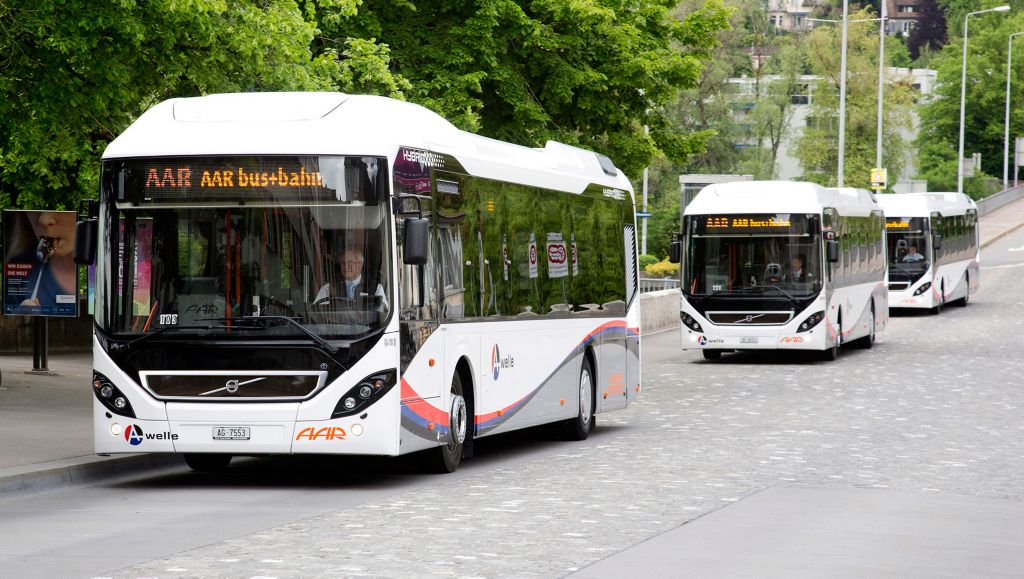 Three white Volvo hybrid buses driving down a street