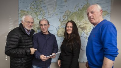 Sjefen sjøl og gode medarbeidere foran et verdenskart. Foto. 