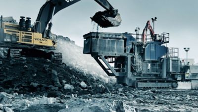 Yellow Volvo Group excavator emptying its ladle full of stones into a stonecrusher