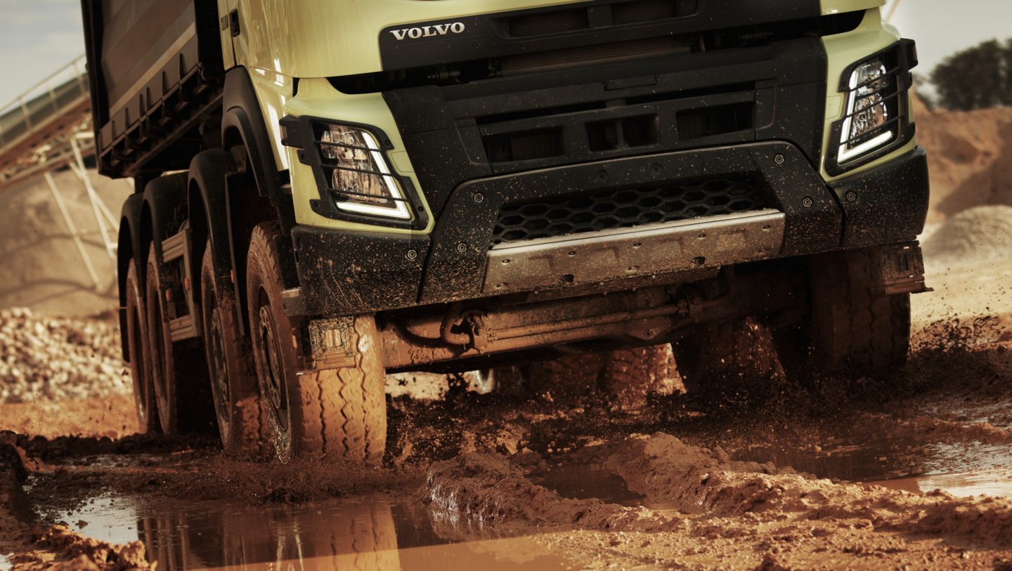 Pearl white industrial Volvo Group truck driving off road through mud and water