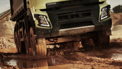 Perlweißer Lkw der Volvo Group fährt im Gelände durch Schlamm und Wasser