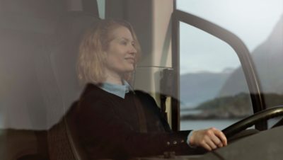 Female bus driver behind the steering wheel with coast in the background