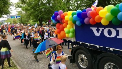 Folk marscherar med Prideflaggor bredvid en blå Volvolastbil