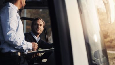 Miespuolinen linja-autonkuljettaja puhuu kollegansa kanssa linja-autossa