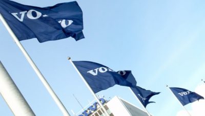 Na wietrze łopoczą cztery flagi Grupy Volvo, w tle widać budynek Volvo