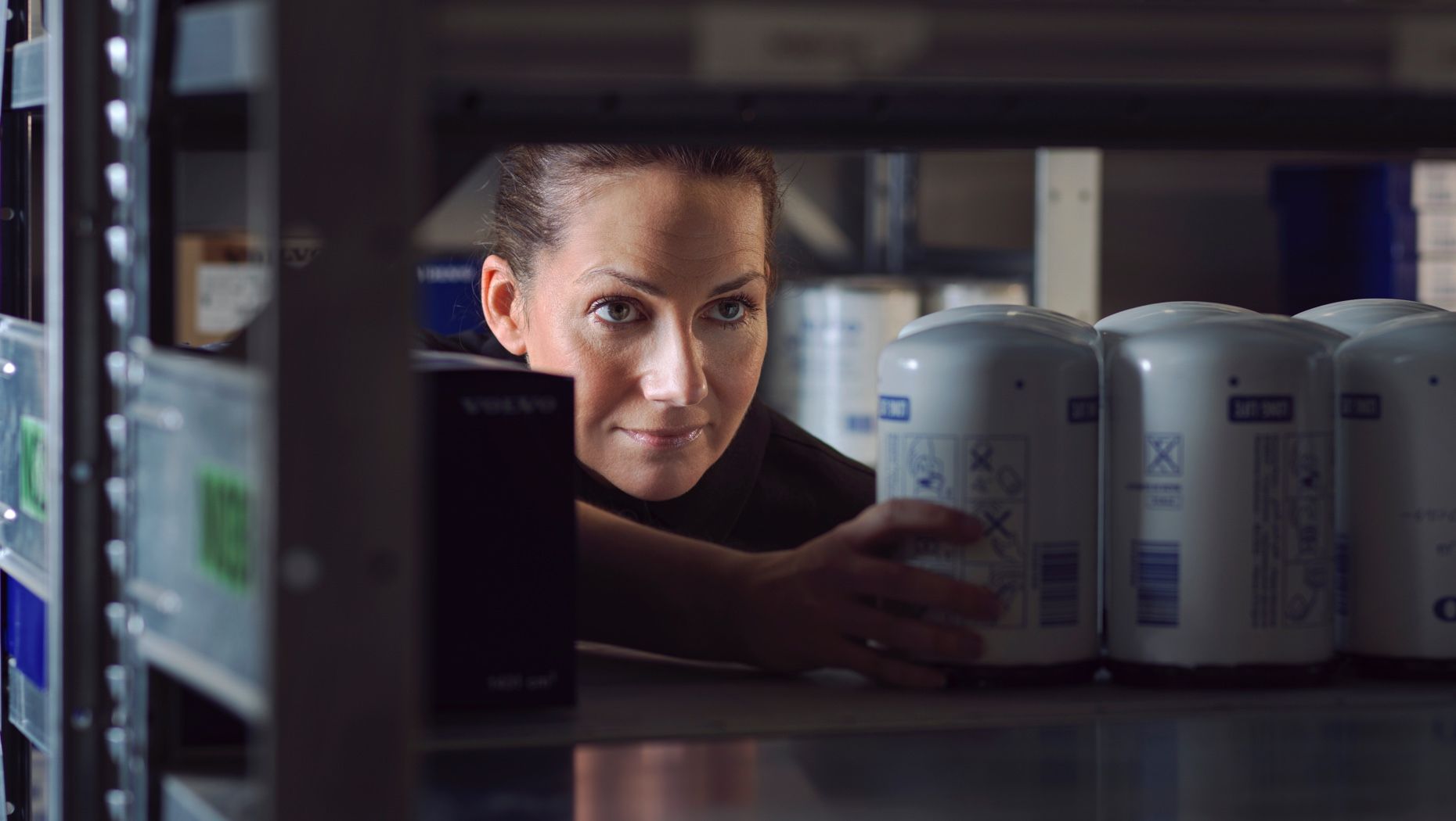 A woman looking through shelves and reaching for a can.