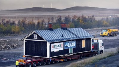 Side view of the Kiruna museum being transported with windmills in the background