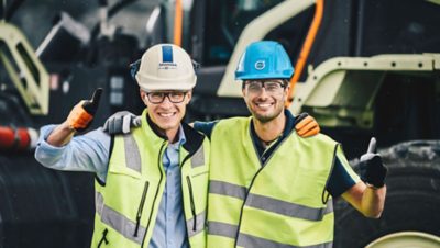 Volvo construction equipment worker and Skanska worker with their arms around each other giving the thumbs up