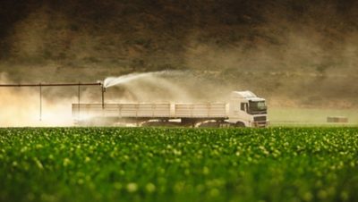 A Volvo FH drives past a green field being watered with a sprinkler