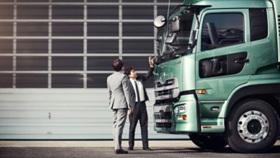 Two japanese Volvo Group employees inspecting a green UD truck