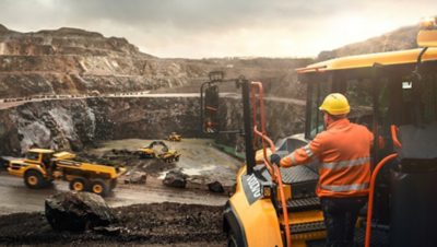 Worker standing on the step of a yellow Volvo Group truck overlooking an excavation site