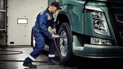 Volvo Group worker in a blue overall tightening the wheel bolts on a blue-green Volvo truck