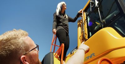 Person pekar på en kvinna som står på en gul anläggningsmaskin