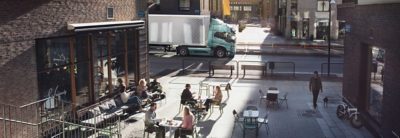volvo Truck driving in a city passing a cafe with people