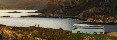 To personer og en buss på en vei med en fjord i bakgrunnen