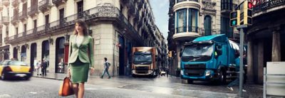 A crossing filled with people and two Volvo trucks waiting for the light to turn green