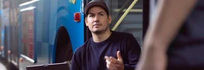En værkstedstekniker i samtale med ikke-synlig person foran en bus. 
