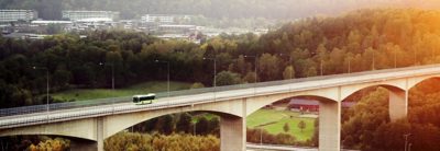  A Volvo bus travels across a bridge, surrounded by nature and with a city in the background.