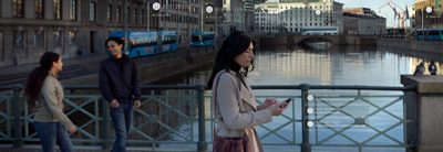 Woman crossing a bridge over a city canal. Two pedestrians in the periphery. Graphics overlay the photo.