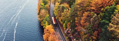 Autobus à étage sur une route au bord d'un lac et d'une forêt aux couleurs automnales