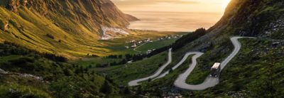 Bus on a meandering road leading down a steep valley towards the sea at dawn