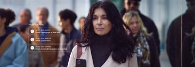 A woman in the foreground holding her mobile in a reading position. Behind her a crowd that is out of focus.