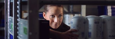 A woman looking through shelves and reaching for a can.