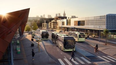 Three different versions of Volvo’s electric city buses at a bus stop. One of the buses is being quick-charged via a pantograph at a charging station.