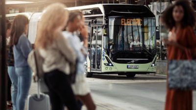 Pearl white Volvo Group bus going towards Lindholmen Science Park on a road surrounded by outdoor restaurant seatings