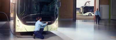 Un autobús en el depósito. Un conductor se dispone a cargar las baterías del autobús.