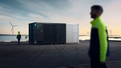 BESS from Volvo Energy stands at a port, one man is seen walking past and a woman is walking next to it.