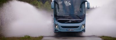 Un autocar de primer nivel de Volvo recorriendo una carretera húmeda durante una prueba de seguridad y rendimiento a escala real, con agua salpicando por los laterales.