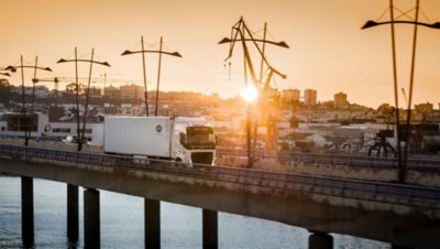 El Volvo FH con I-Save cruza un puente al atardecer con una ciudad española al fondo