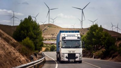 Egy tesztelést végző teherautó az úton Spanyolországban, a háttérben szélerőművekkel