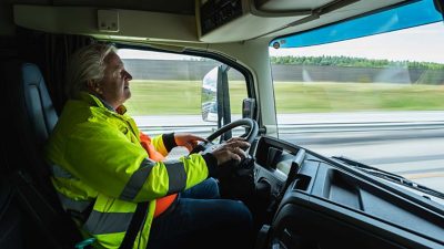 Mann i førerhuset på lastebil på motorvei. 