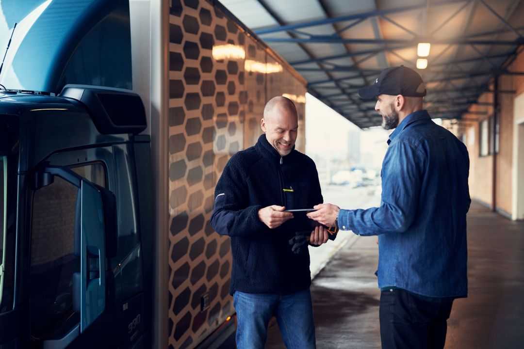 Men talking in front of a truck watching a tablet