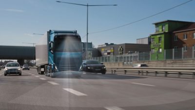 Blauer Volvo-Lkw nutzt Pilot Assist auf der Autobahn, wobei das Sensorfeld visualisiert wird, während er den Abstand zu nahen Fahrzeugen im Verkehr einhält.