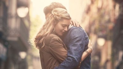 Pareja joven abrazándose en una ciudad con autobuses Volvo eléctricos, expresando amor y tranquilidad.