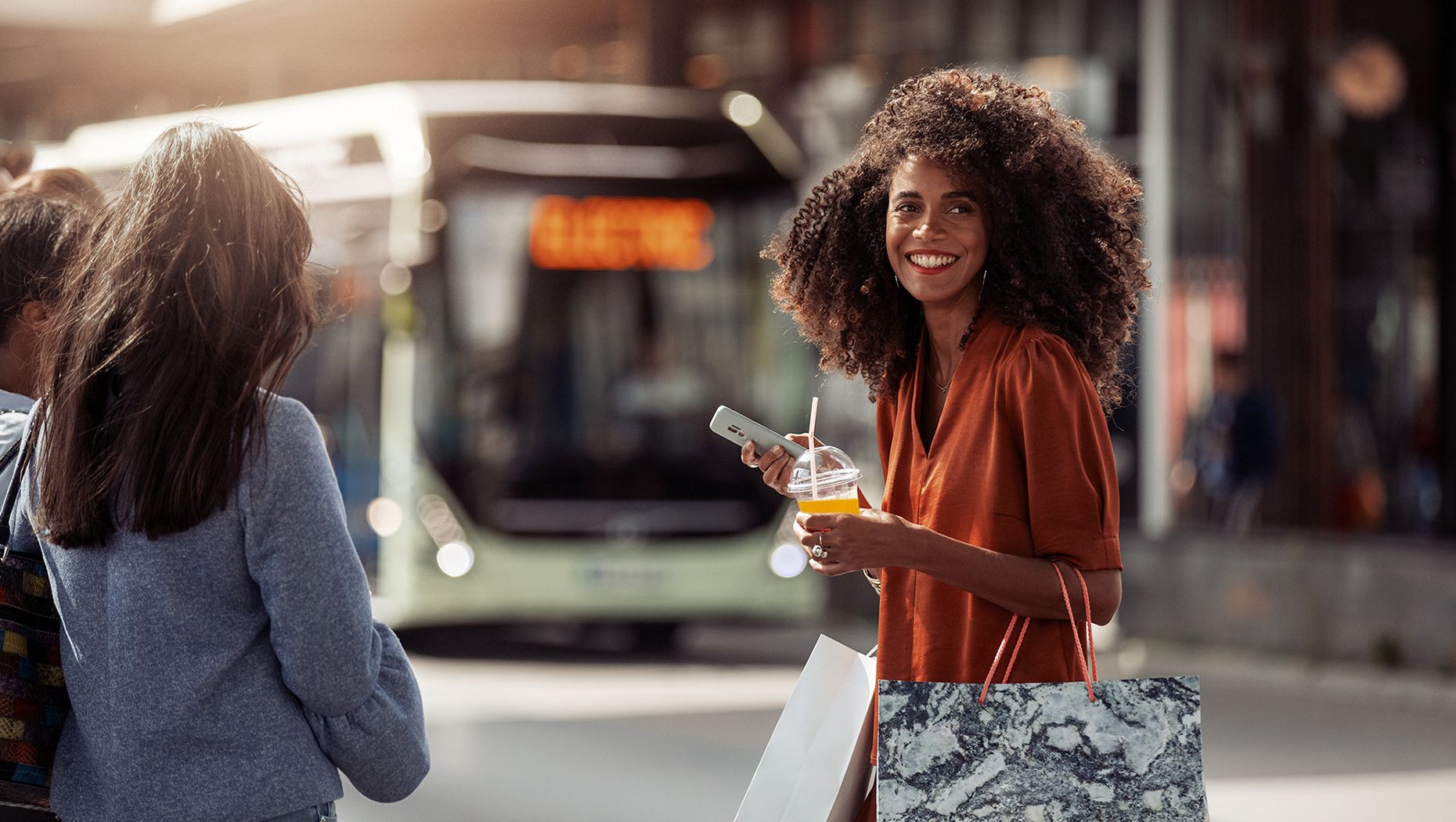 Happy woman smiling when crossing the street in front of an electric Volvo city bus.