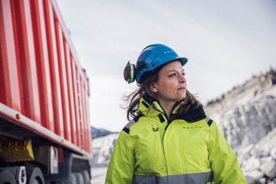 a woman wearing a Volvo safety helmet and safety jacket near a read Volvo FH truck in Brönnöy