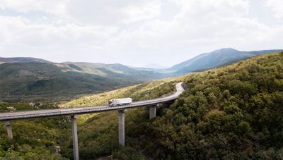 A connected and autonomous truck from Volvo driving on a high bridge running through a green landscape. There's no other traffic on the road.