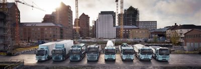 Rad elektrických nákladných vozidiel Volvo vedľa seba pred panorámou mesta.