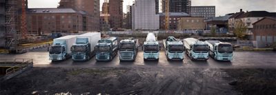 A range of Volvo electric rigid trucks side by side in front of a cityscape.